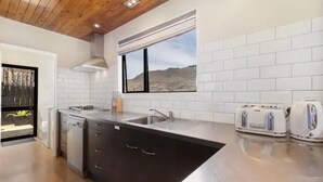 A modern kitchen with white subway tiles, a black island with drawers, a stainless steel sink, and a window with a desert view.