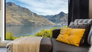 A room with a view of a lake and mountains, a sofa with a yellow pillow, and a window with curtains.