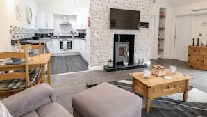 A modern living room with a fireplace, a kitchen with white cabinets, and a dining area with a table set for two. - Kingfisher Lodge (Great Yarmouth)