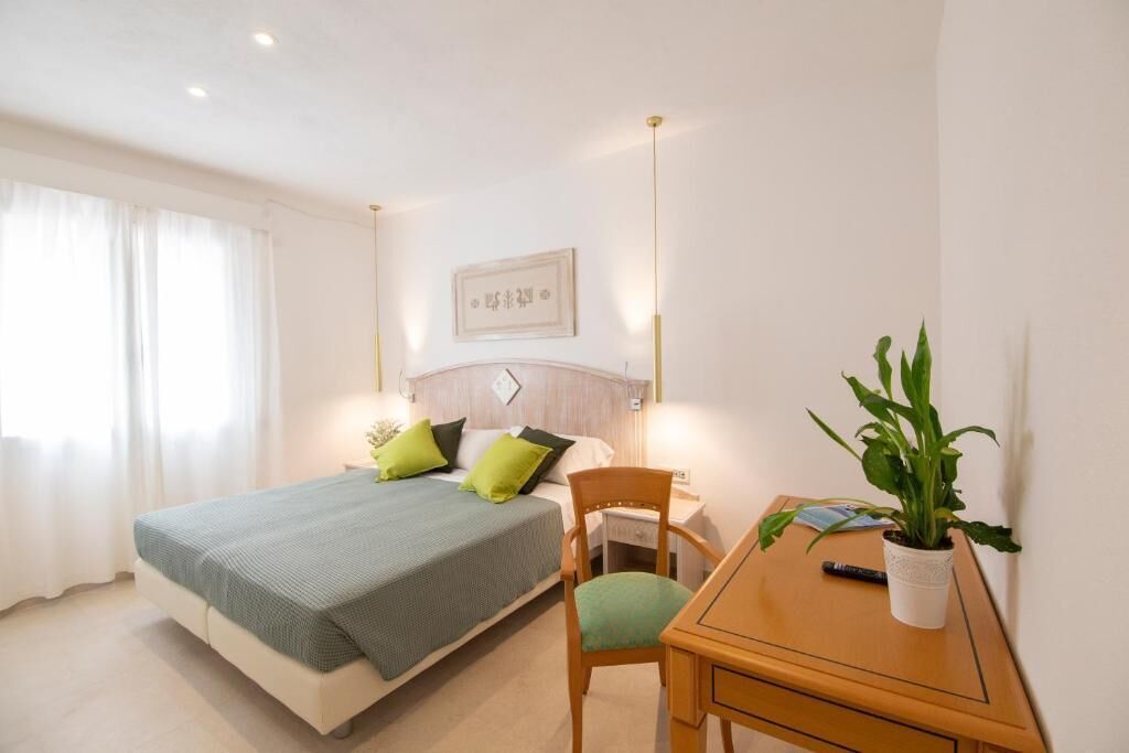 Un dormitorio con cama, mesita de noche, silla y una planta en maceta.