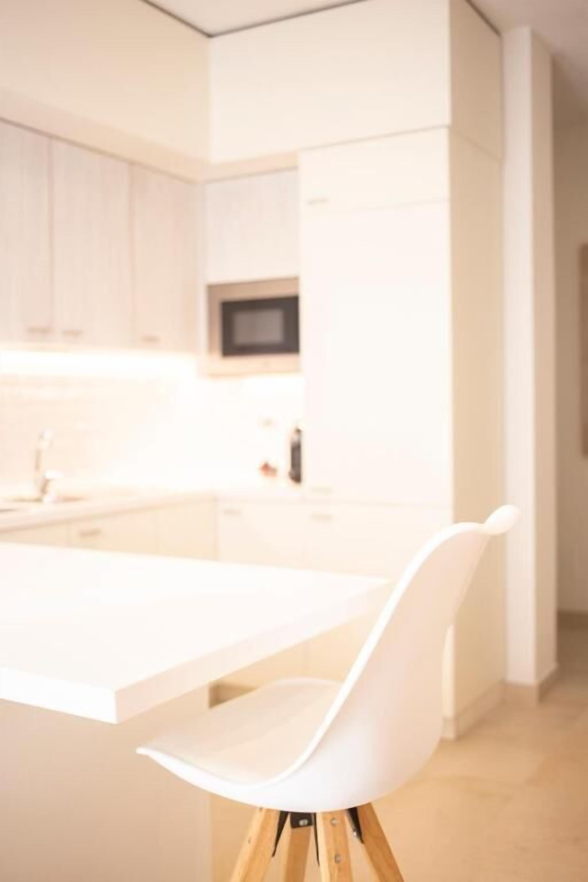 A modern kitchen with white cabinetry, a central island, and a white chair.