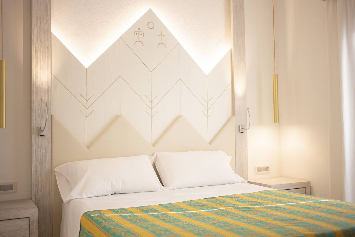 A hotel room with a bed, a bedside table, and a wall with geometric patterns.