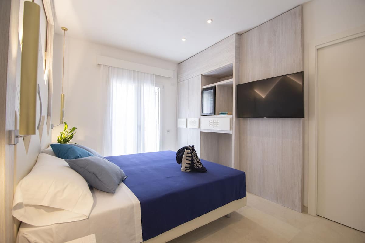 A modern bedroom with a bed, a TV mounted on the wall, and built-in storage.