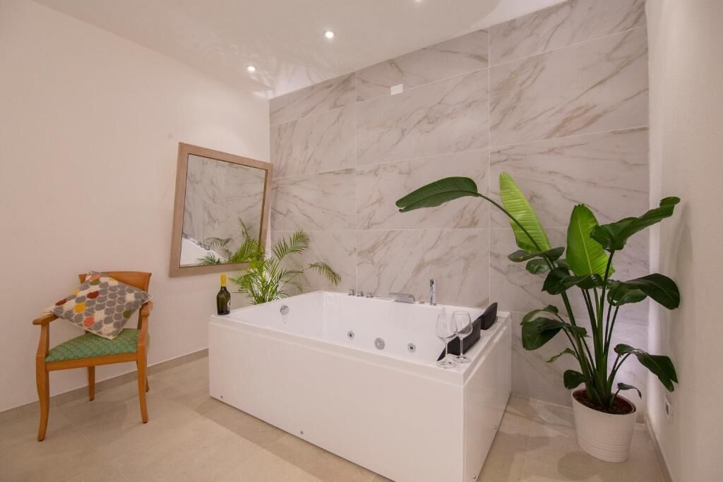 Een moderne badkamer met een ruim bad, een stoel met kussen, een potplant en een ingelijste foto aan de muur.