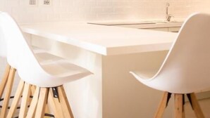 A modern kitchen with white cabinetry, a white countertop, and two white bar stools. - Tabernabè (Tortoli)