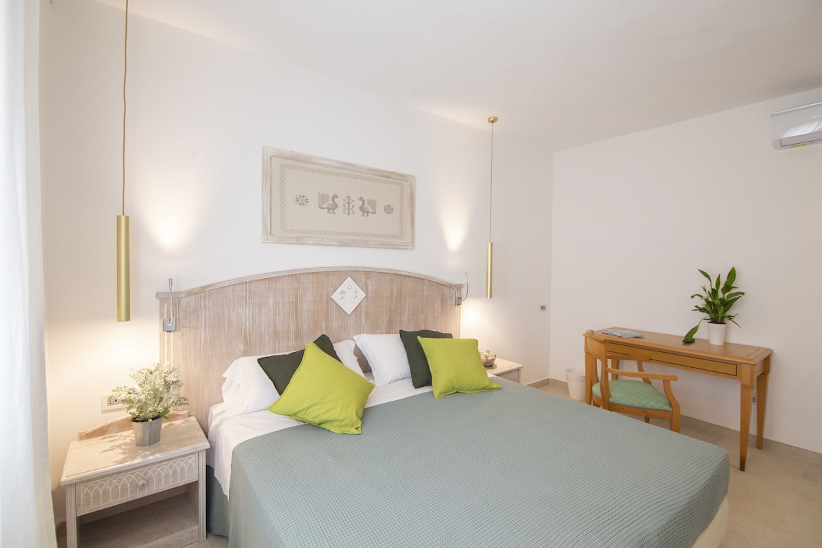 A neatly arranged bedroom with a bed, bedside tables, a desk, and a potted plant.