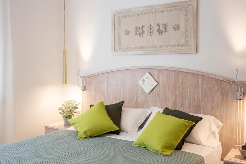 A neatly made bed with green and white bedding, a wooden headboard, and a wall-mounted artwork.