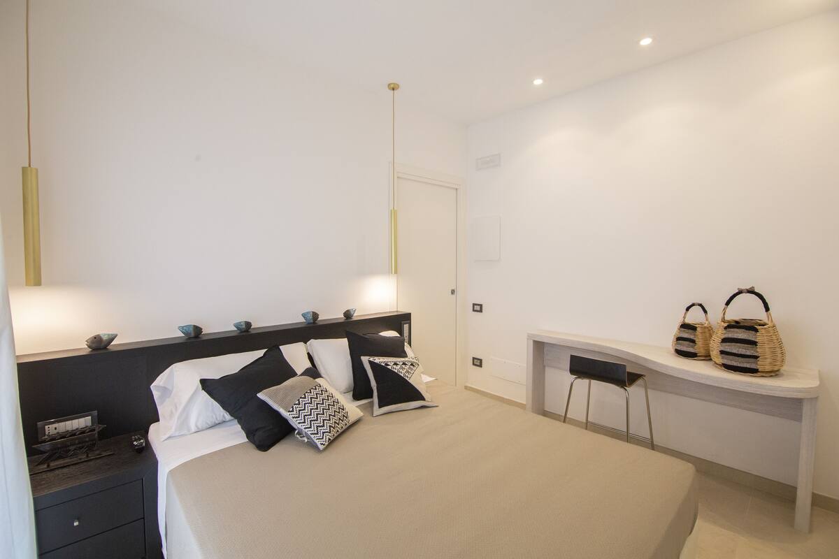 A modern bedroom with a bed, bedside tables, a desk, and a chair.
