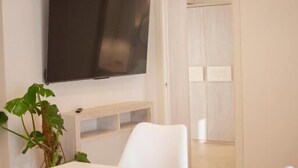 A modern, minimalist room with a flat-screen TV mounted on the wall, a white table, and two white chairs. - Tabernabè (Tortoli)