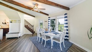 Zona pranzo con soffitto in legno, sedie bianche e tappeto blu.