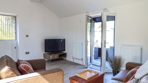 A modern living room with a flat-screen TV on a wooden stand, leather sofas, a wooden coffee table, and a sliding glass door leading to an outdoor area. - Tan Llech (Harlech)