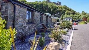 A stone building with large windows, a gravel driveway, and a view of a hill with a castle-like structure in the background. - Tan Llech (Harlech)
