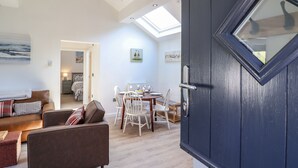 A modern living room with a sofa, dining table, and chairs. There is a skylight above the dining area and a dark wooden door with a window. - Tan Llech (Harlech)