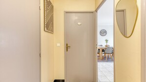 A hallway with a closed door, a wall-mounted clock, and a dining area visible through the door.