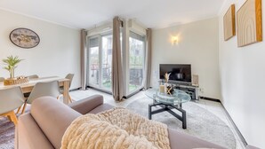 A modern living room with a sofa, a glass coffee table, a TV, and a dining area with a table and chairs.