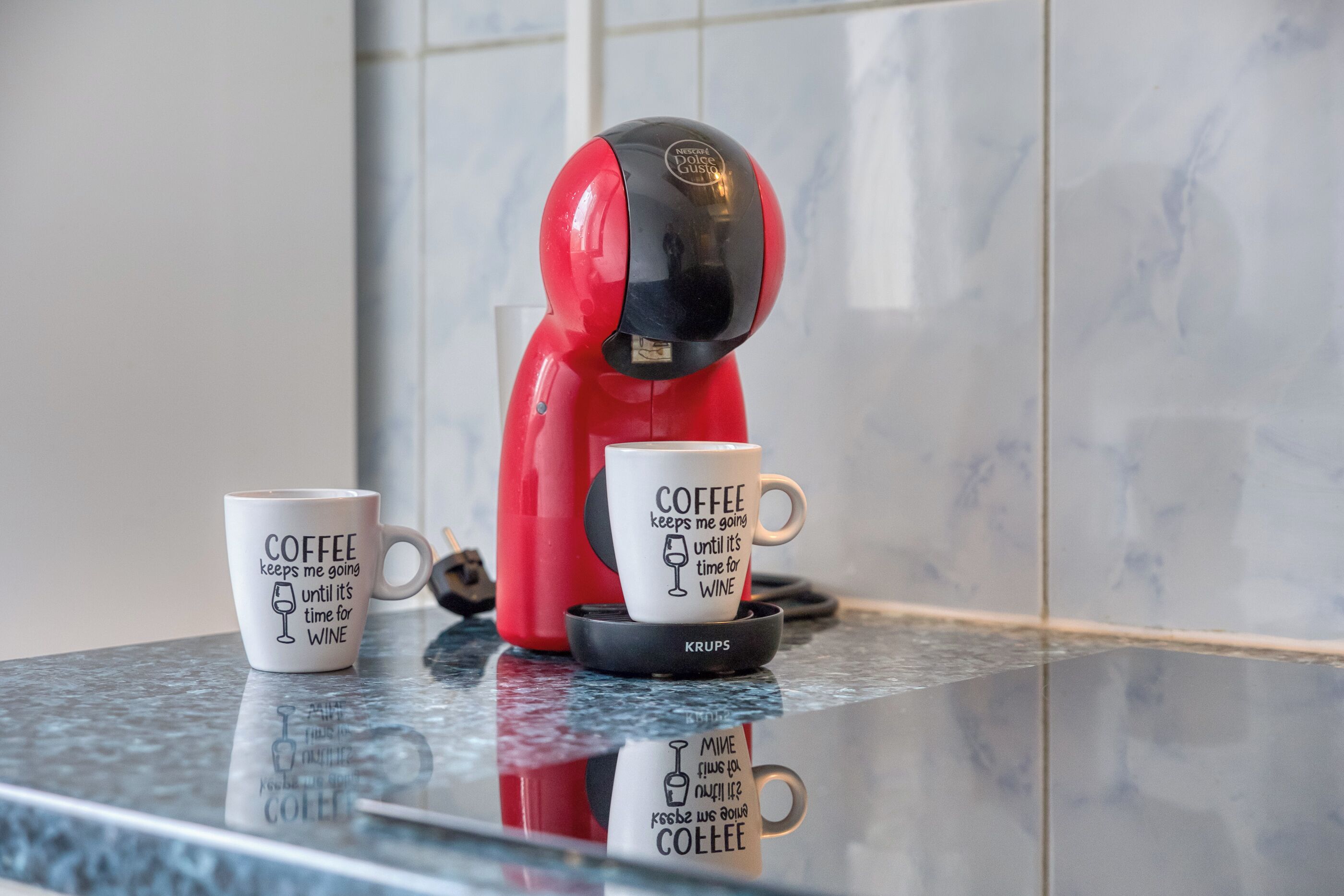 Een rode koffiezetapparaat met twee koffiekopjes op een aanrecht.