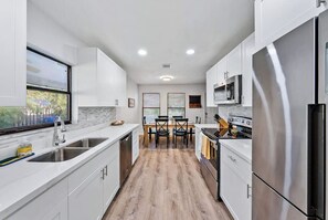 A modern kitchen with white cabinets, stainless steel appliances, and a wooden floor.