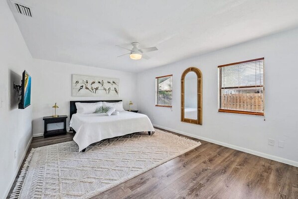 A bedroom with a bed, a ceiling fan, a painting, two bedside tables, and a large mirror.