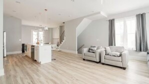 Een ruime woonkamer met een keuken, twee banken, een eettafel en een trap.