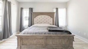 Een slaapkamer met een groot bed, een houten hoofdbord en grijze gordijnen.
