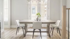 Een eethoek met een houten tafel, twee witte stoelen, een hanglamp en een potplant.