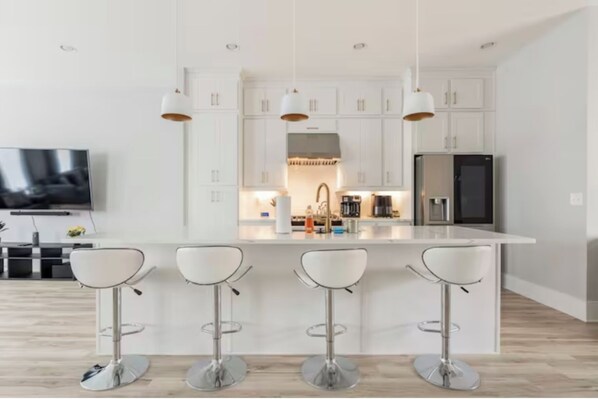 A modern kitchen with white cabinets, a central island with bar stools, a built-in oven, and a large refrigerator.