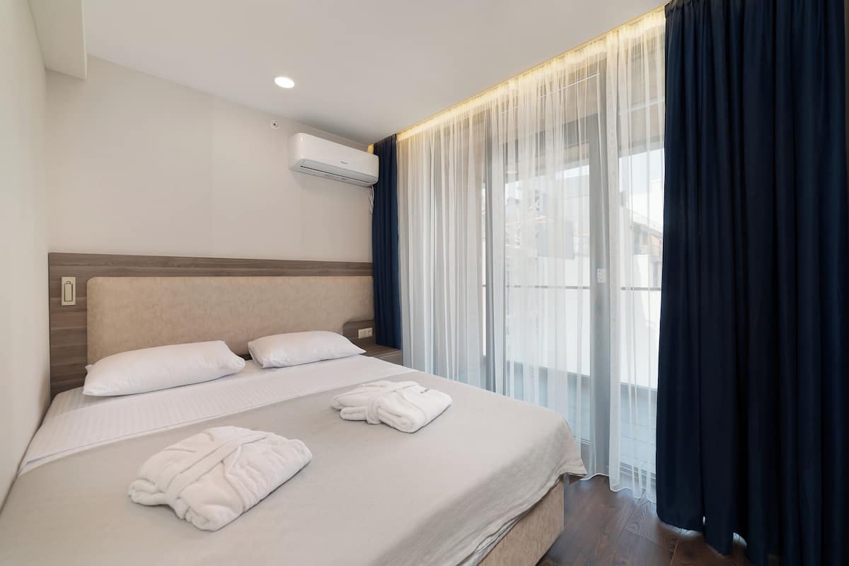Ein Hotelzimmer mit Bett, zwei Kissen, einem gefalteten Handtuch, einer Klimaanlage und transparenten Vorhängen.