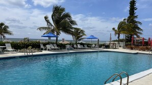 A swimming pool with lounge chairs and umbrellas, surrounded by palm trees. - Beach Front Condo with Ocean View (Freeport)