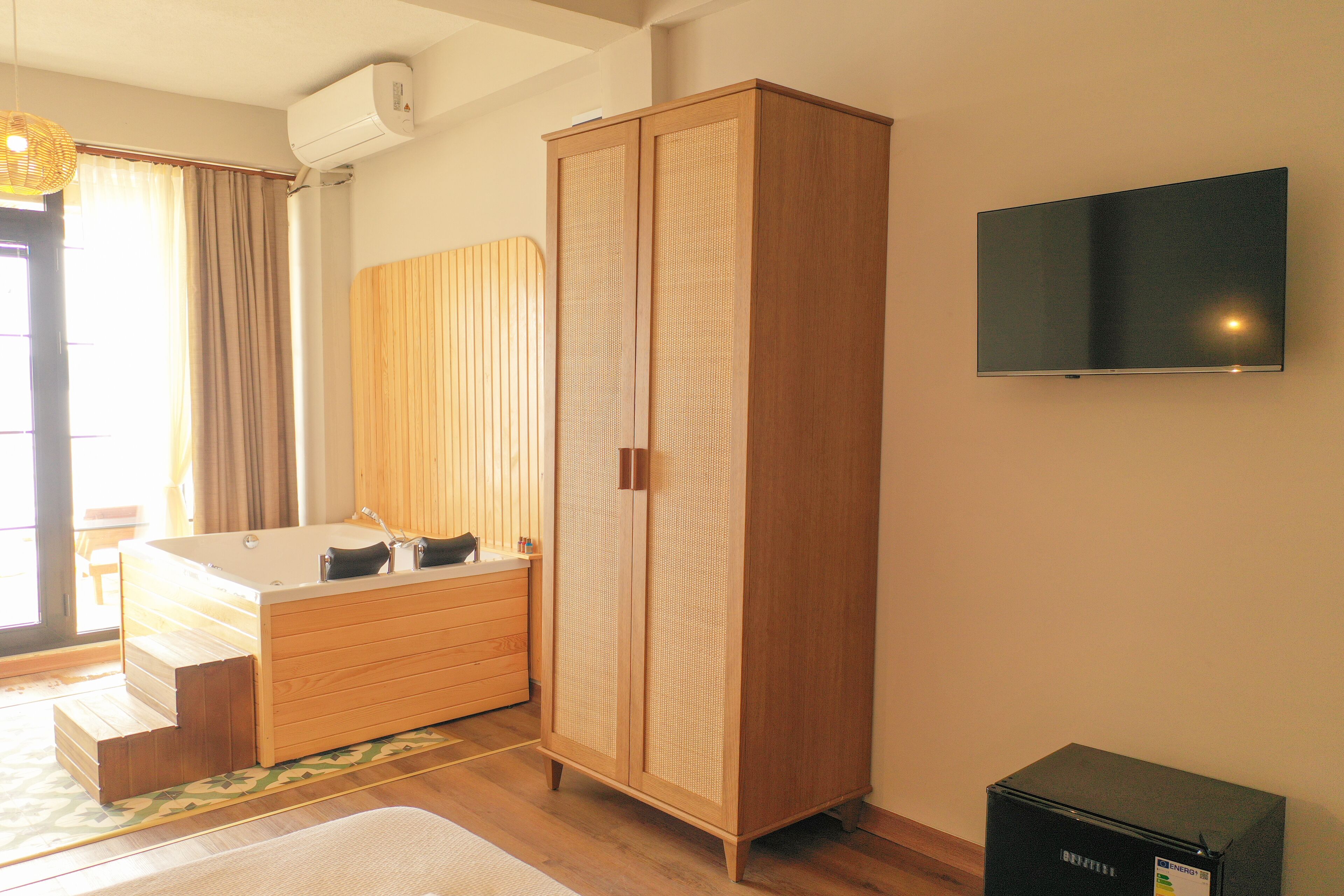 A modern bathroom with a wooden vanity, a bathtub, and a flat-screen TV mounted on the wall.