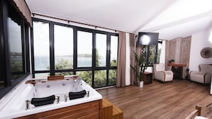 Une pièce spacieuse avec une grande fenêtre, un plancher en bois, une baignoire, deux chaises et une petite table.