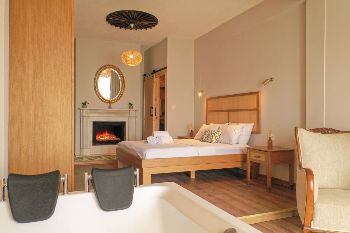 A bedroom with a wooden bed, a fireplace, a large mirror, and two chairs.