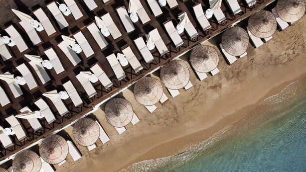 Vue aérienne d’un hôtel situé en bord de mer, avec des rangées de chaises longues et de parasols de plage.