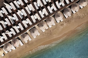 Ein Luftbild eines Hotels direkt am Strand, mit Reihen von Liegestühlen und Sonnenschirmen.