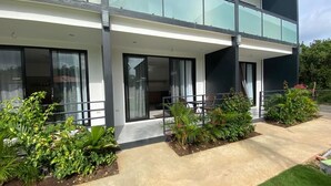A modern two-story building with large glass windows, a balcony with chairs, and a well-maintained garden area.