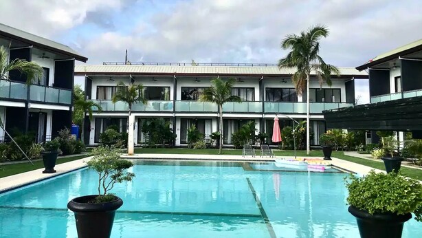 A hotel with a swimming pool, multiple balconies, and palm trees.