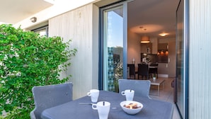 A dining area with a table set for four, a bowl of fruit, and four white cups. - Les Thermes 508 - Appt avec piscine partagée (Concarneau)