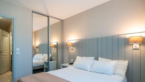A hotel room with a large bed, bedside tables, a mirror, and wall-mounted lamps. - Les Thermes 508 - Appt avec piscine partagée (Concarneau)