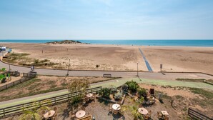 Une vue sur la plage avec une promenade dallée, un espace extérieur aménagé avec des sièges et une route qui longe la plage.
