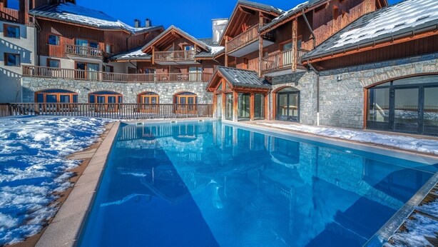 A hotel with a swimming pool, stone walls, wooden balconies, and a clear blue sky. - Les Alpages du Corbier C301 - Piscine partagée (Villarembert)