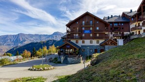 A multi-story hotel with a stone facade, wooden balconies, and a ski resort backdrop. - Les Alpages du Corbier C301 - Piscine partagée (Villarembert)