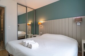 Quarto de hotel com uma cama grande, espelho, abajures e um guarda-roupa.