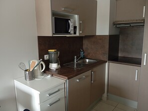 Cocina compacta con microondas, lavamanos y cafetera.