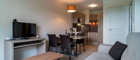 Una sala de estar moderna con un sofá, un televisor, una mesa de madera y un comedor con sillas y una mesa.
