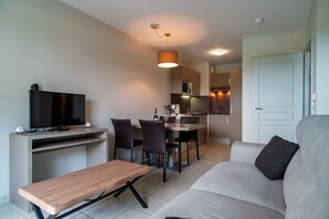 Uma sala de estar moderna com sofá, televisão, mesa de madeira e área de jantar com cadeiras e mesa.