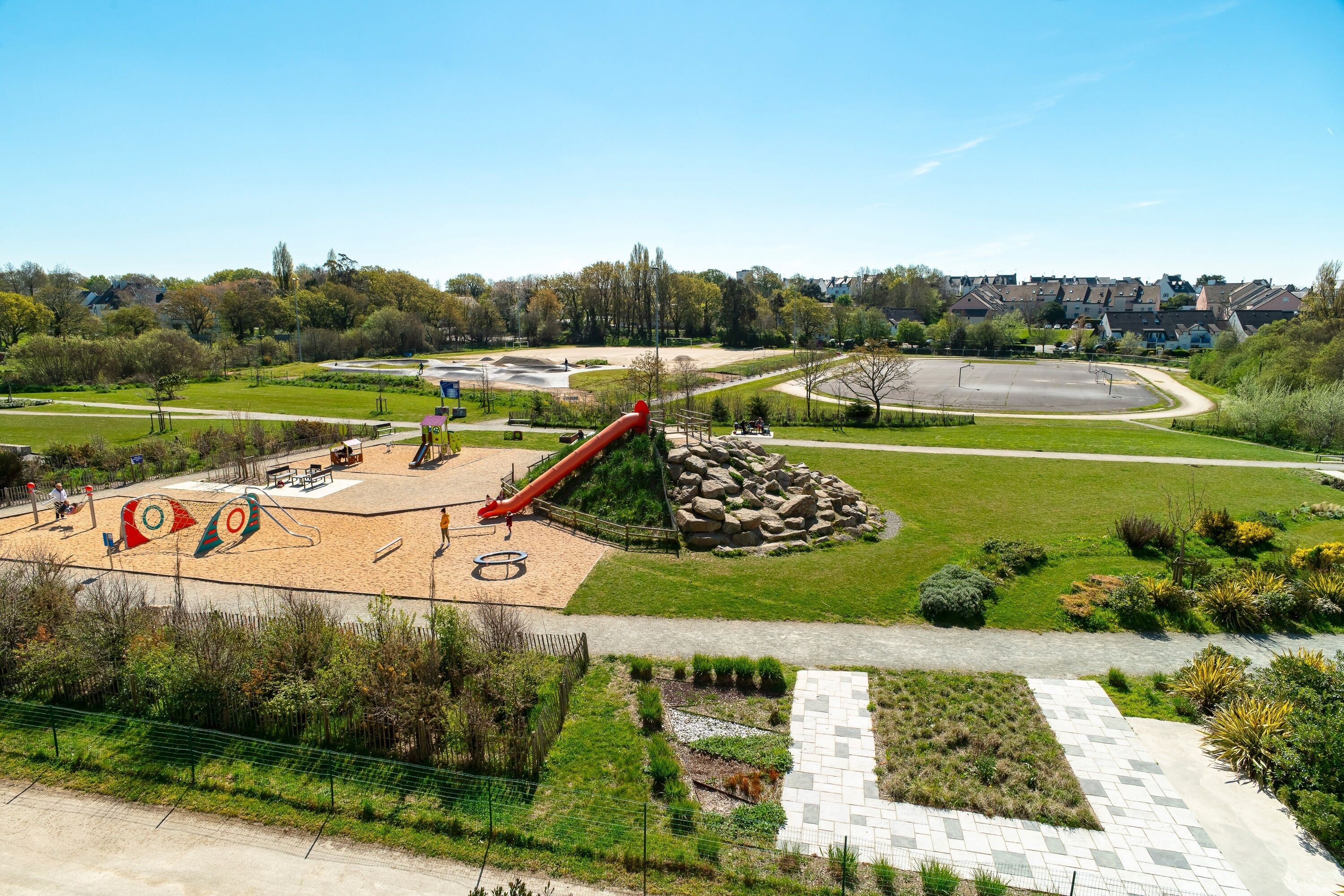 A playground with a slide and sand area, surrounded by landscaped gardens and pathways.