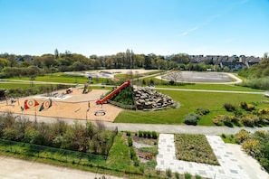 Un parque con un patio de recreo, un tobogán rojo y un sendero pavimentado.