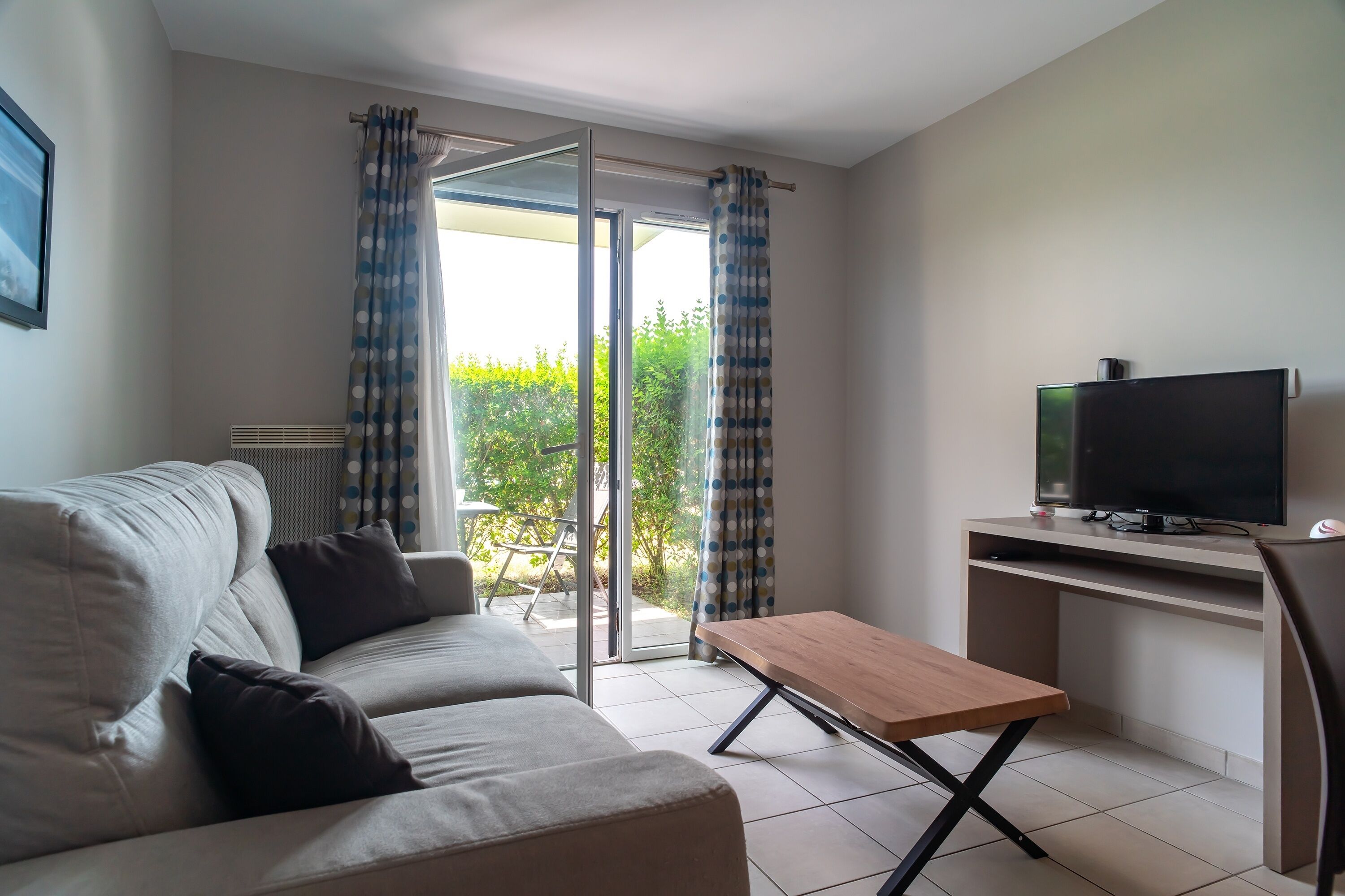 A modern living room with a sofa, a wooden coffee table, a TV on a stand, and a sliding glass door leading to a balcony.