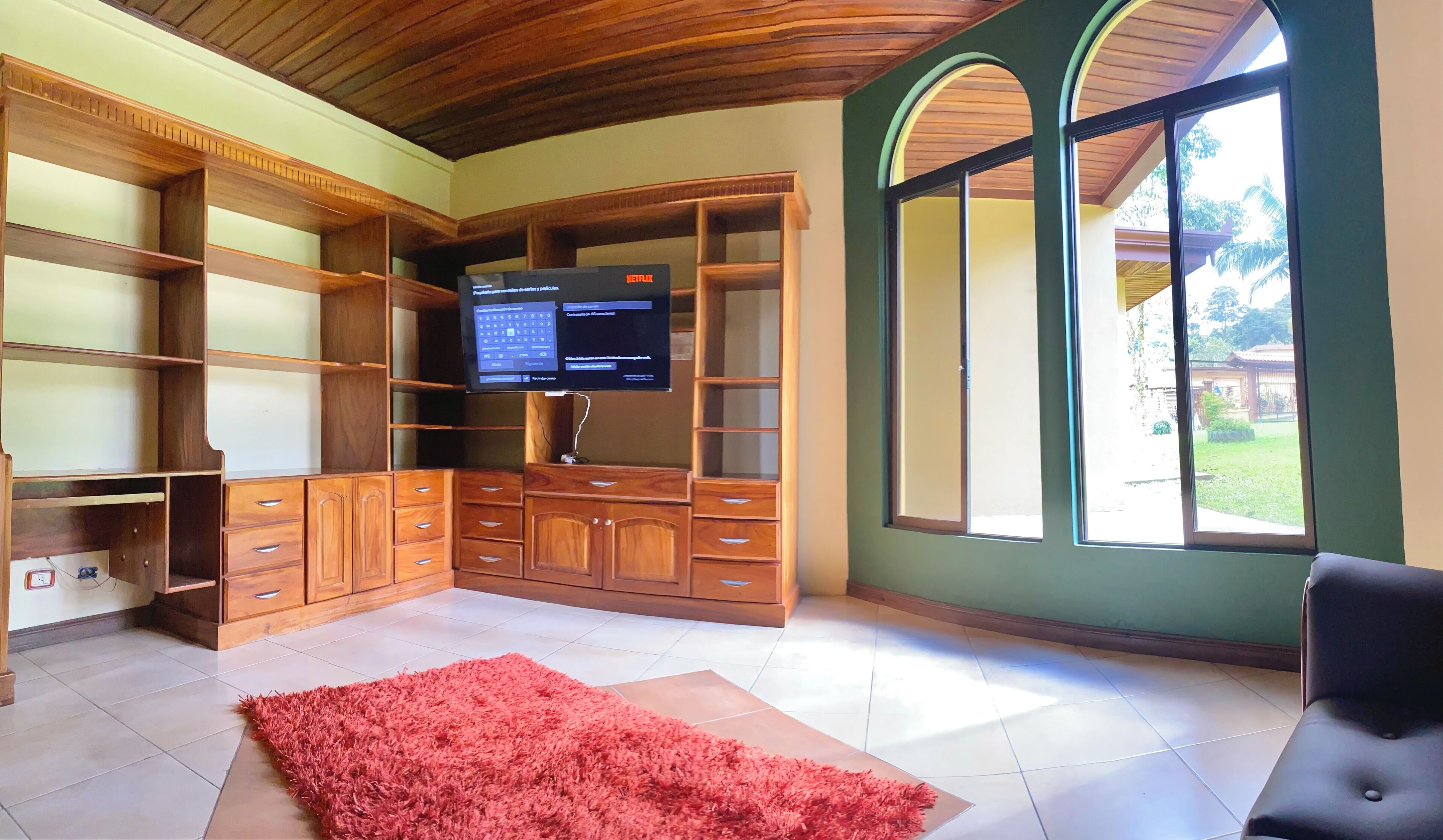 Una habitación amplia con un mueble grande de entretenimiento de madera, un televisor de pantalla plana y un ventanal con vistas al exterior.