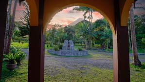 An archway framing a view of a landscaped area with a central rock feature and palm trees. - Mansion Arenal  (La Fortuna)