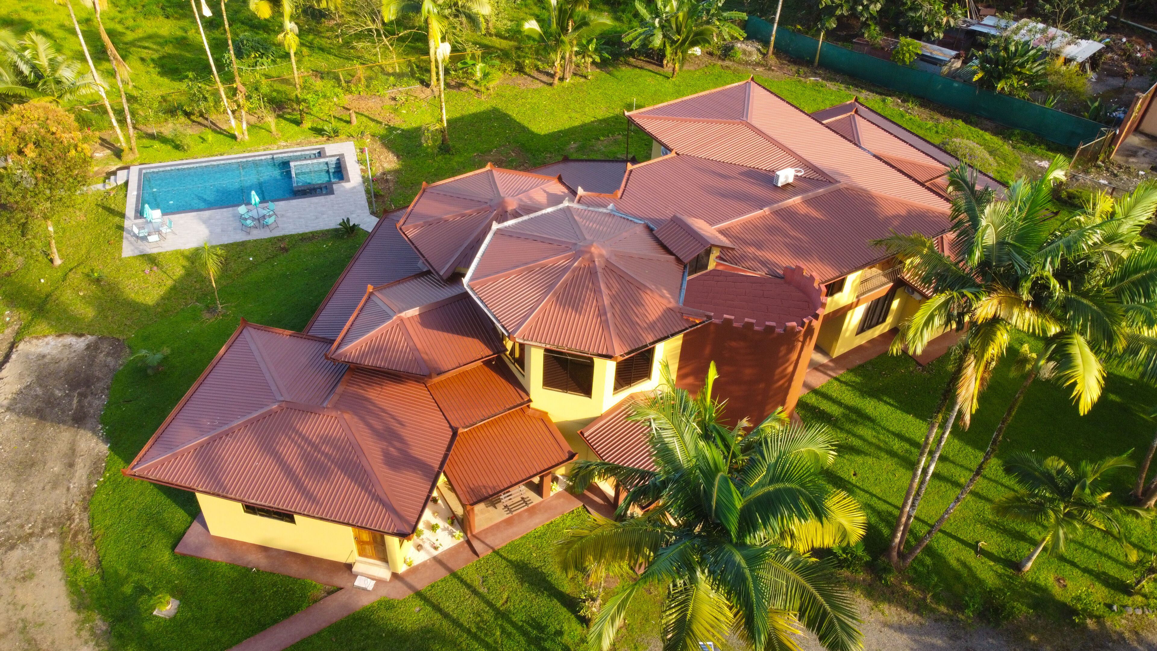 A large, multi-roofed building with a swimming pool and lush greenery.